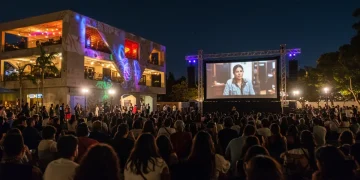 Público diverso en un festival de cine mexicano al aire libre en 2026, celebrando la cultura y el cine. Personas de diferentes edades y orígenes disfrutan de una proyección nocturna, con luces festivas iluminando el ambiente.